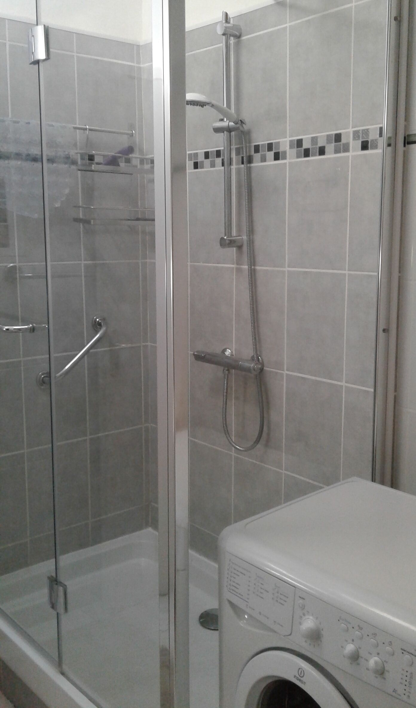 A bathroom with a glass-enclosed shower, a washing machine, and tiled walls.