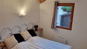 Un dormitorio con una cama grande, vigas de madera, una mesita de noche, una lámpara de pared y una ventana con cortinas.