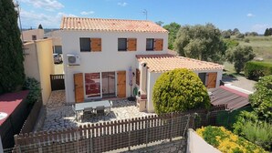 Una casa de dos pisos con techo de tejas, un patio de piedra y un jardín cercado.
