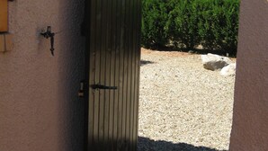 Una reja metálica cerrada da acceso a un camino de grava con un seto al fondo.