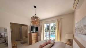 Een slaapkamer met een bed, een televisie op een houten dressoir, een douche en uitzicht op een zwembad.
