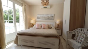 Een slaapkamer met een groot bed, twee nachtkastjes, een rieten stoel en een raam met gordijnen.