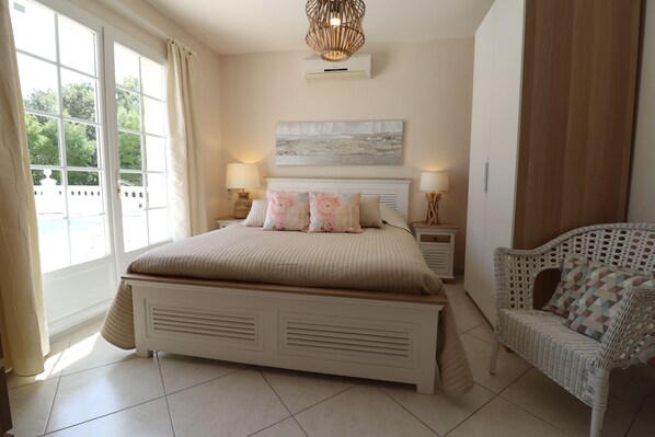 A bedroom with a large bed, two bedside tables, a wicker chair, and a window with curtains. - La Cèzenole | Villa 5* air-conditioned Bungalow | Heated pool | Gorges Cèze (Méjannes le Clap)