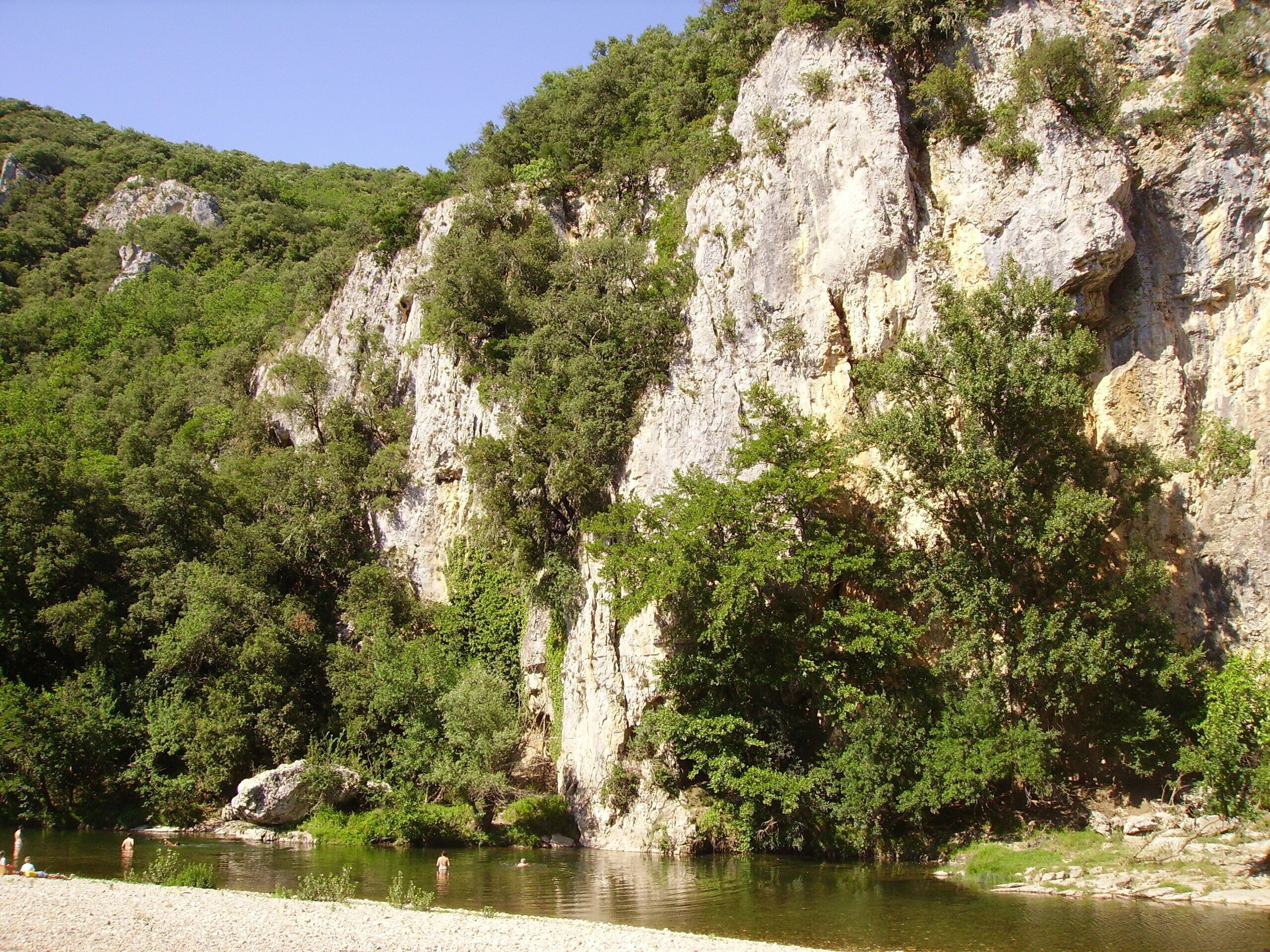 A natural landscape with a river, rocky cliffs, and dense greenery.