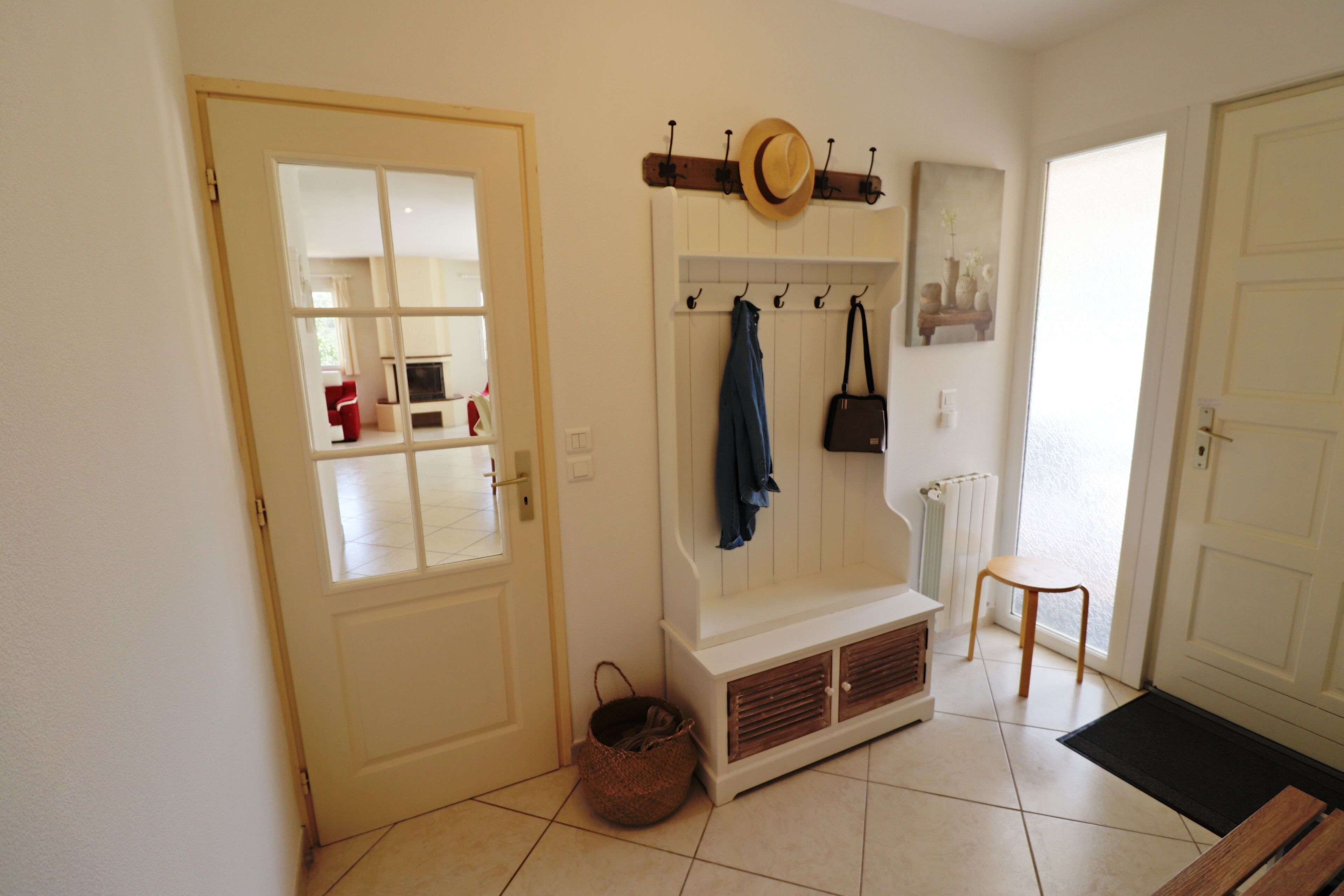 A hallway with a bench, a coat rack, and a door leading to a room.