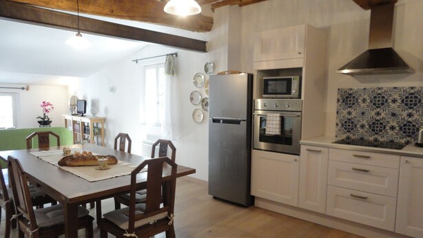 Una cocina con armarios de madera, un refrigerador de acero inoxidable, un horno y un microondas. Hay una mesa de comedor con sillas y un jarrón con flores.
