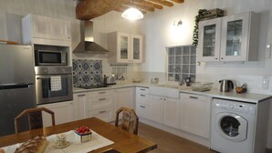Una cocina moderna con armarios blancos, electrodomésticos de acero inoxidable, una mesa de comedor de madera y una lavadora integrada.