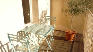 Un balcón con una mesa y sillas de metal, una planta en maceta y una vista de un edificio al fondo.