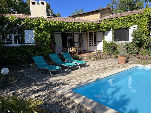 Zona de piscina con piscina, sillas de descanso y un patio cubierto con mobiliario exterior.