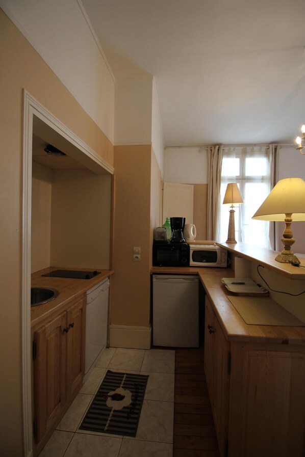 A compact kitchen with wooden cabinets, a microwave, a coffee maker, and a small refrigerator.