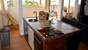 A compact kitchen with a sink, stove, and a dining area with a chair and table. - F2 Panoramic view sea, mountain and swimming pool view of the residence (Le Carbet)