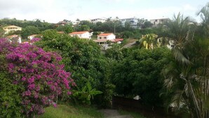 A residential area with houses, lush greenery, and a prominent pink flowering bush. - F2 Panoramic view sea, mountain and swimming pool view of the residence (Le Carbet)