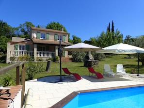 A swimming pool with lounge chairs and umbrellas, a stone fireplace, and a house with a balcony and green shutters. - VILLA comfortable not overlooked, calm close to the city (Uzès)