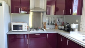 A compact kitchen with a microwave, gas stove, and various utensils hanging on the wall.