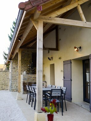 Un'area pranzo all'aperto riparata, con parete in pietra, travi in legno e un'atmosfera rustica.