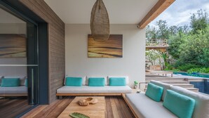 A modern outdoor living area with a wooden bench, a sofa with teal cushions, and a hanging light fixture. - Incredible 5* villa near Cala Rossa (Porto-Vecchio)