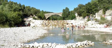Une rivière traversée par un pont de pierre, entourée d’arbres et de rochers.