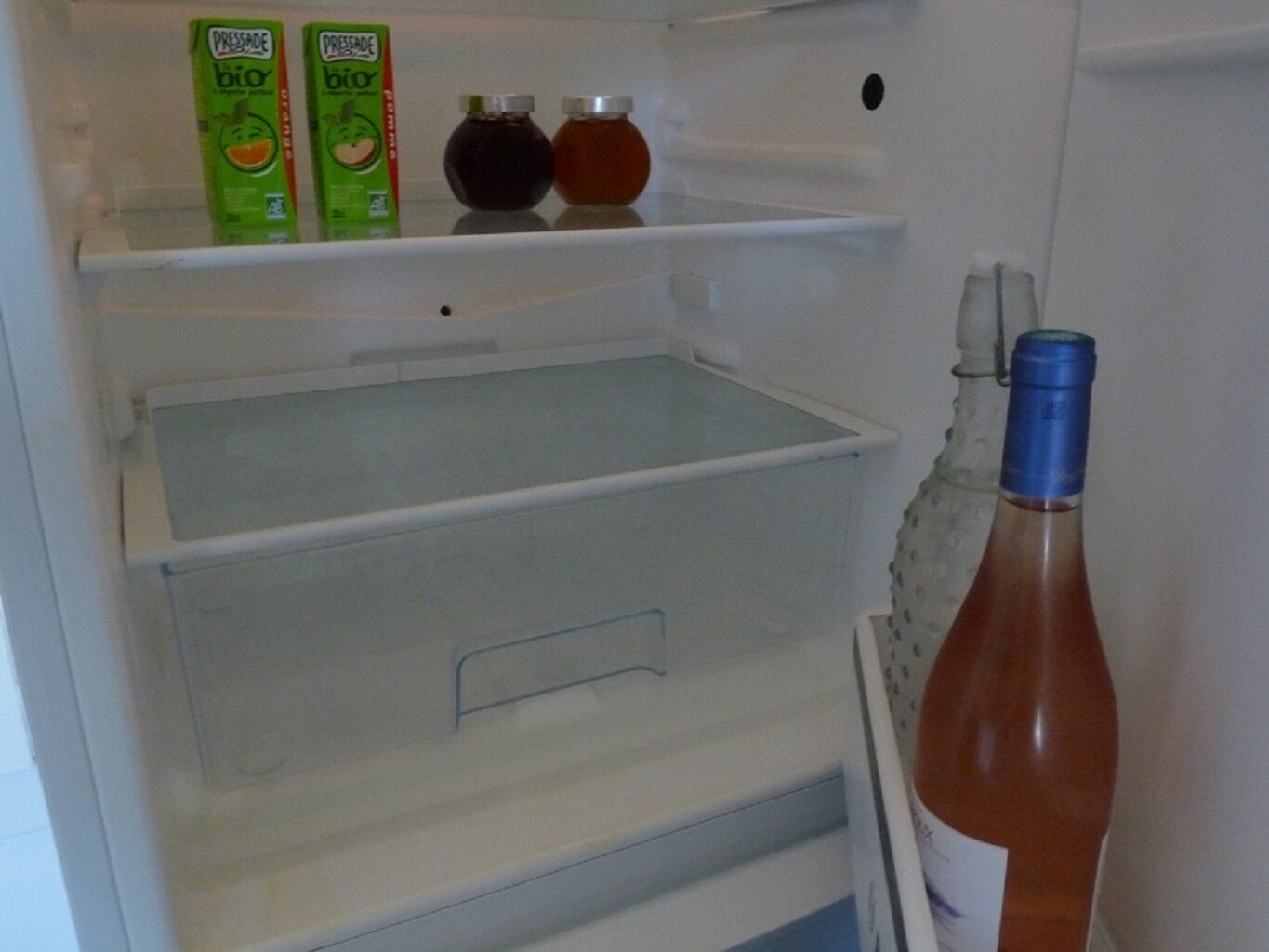 An open refrigerator with two boxes of 'Pressade bio' juice, two bottles of dark liquid, and a bottle of red liquid with a blue cap.