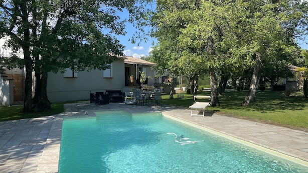 A swimming pool with a patio area, surrounded by trees and a building with a tiled roof. - Drôme provençale, nature, outdoor swimming pool and spas  (La Baume-De-Transit)