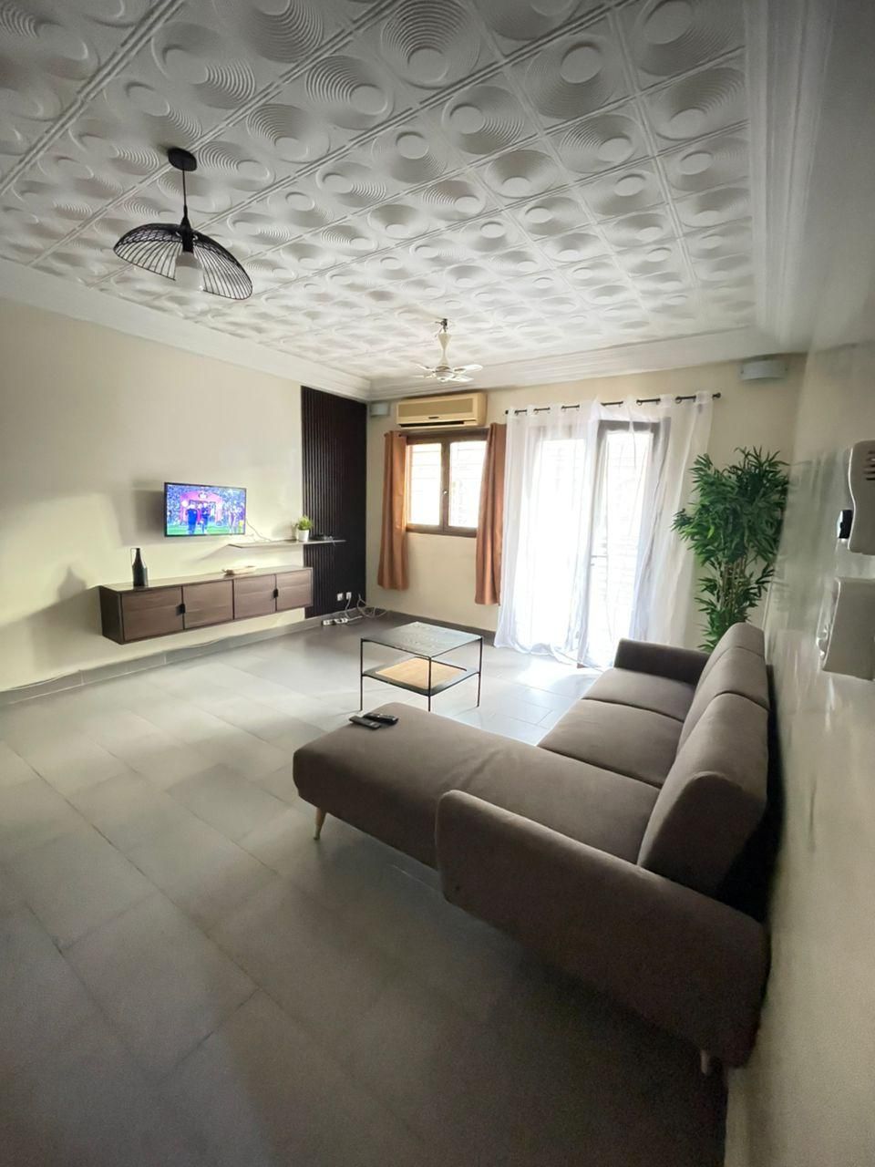 Un salon avec un canapé, un téléviseur, un ventilateur de plafond et une fenêtre avec des rideaux.