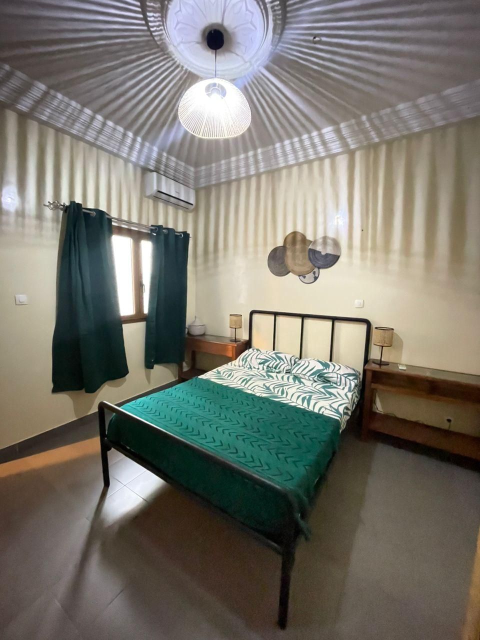 A room with a bed, a ceiling fan, a wall-mounted air conditioner, and a window with curtains.