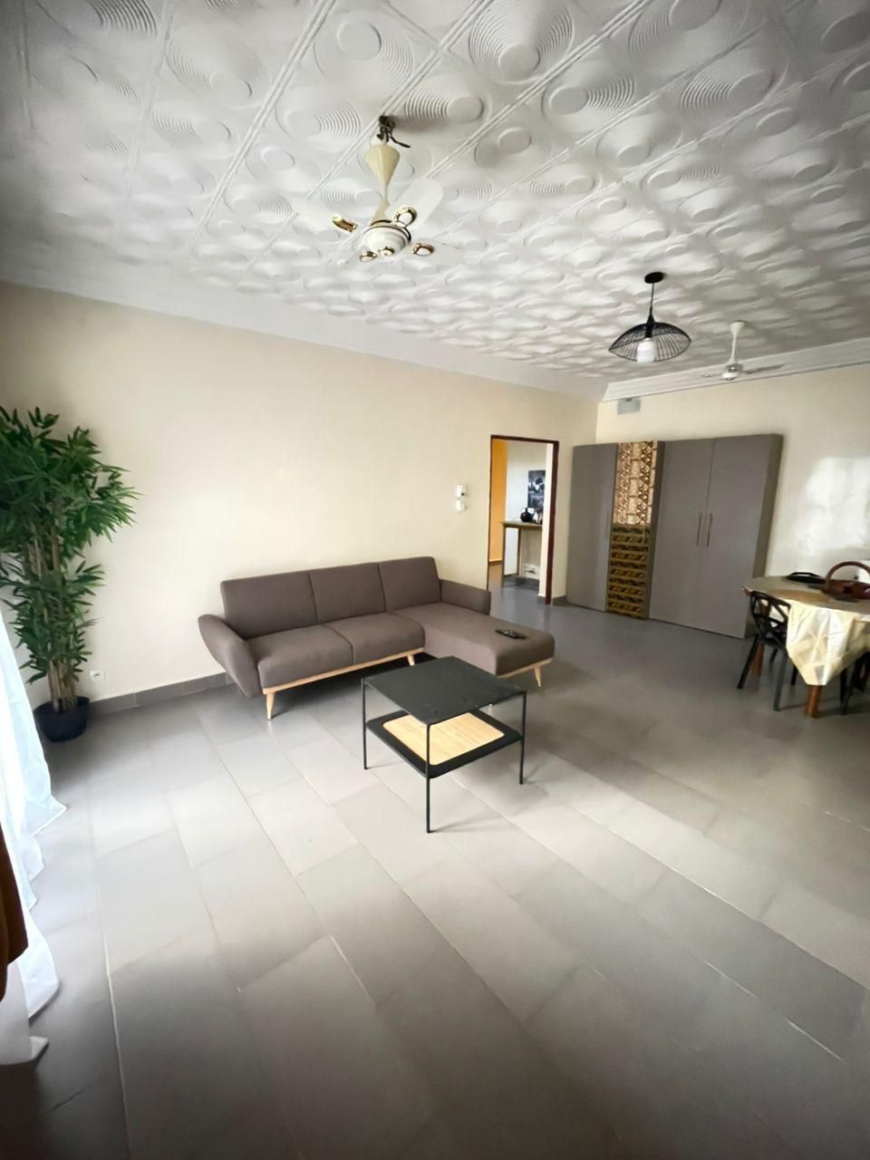 Ampla sala de estar com sofá, mesa de centro, mesa de jantar e teto com padrão decorativo.