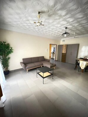 A spacious living area with a sofa, a coffee table, a dining table, and a ceiling with a decorative pattern.