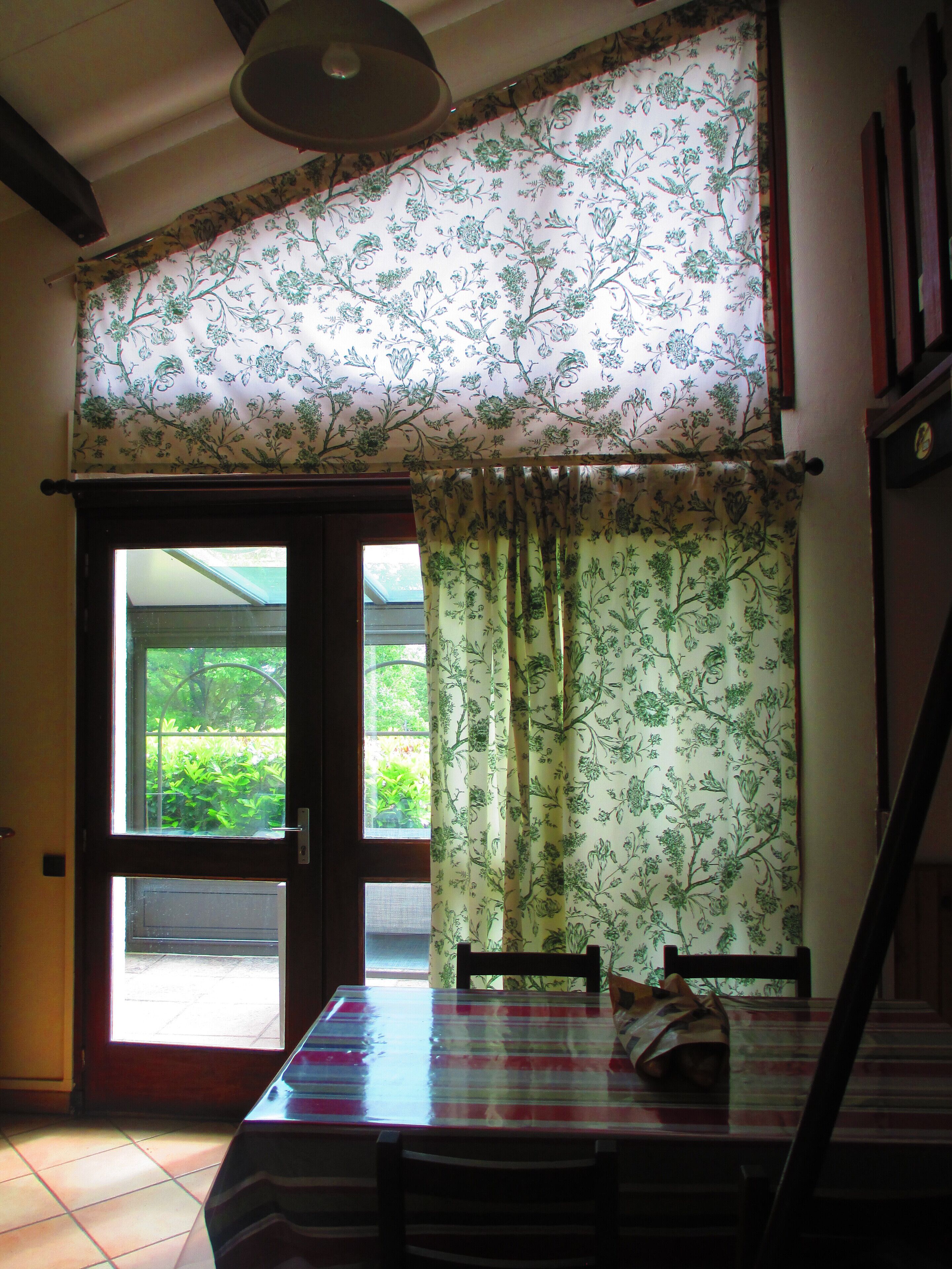 Ein Essbereich mit Tisch und Stühlen, ein Fenster mit Vorhängen und Blick auf Grünfläche.