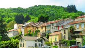 A row of traditional European-style houses with stone facades, set against a backdrop of lush green hills.