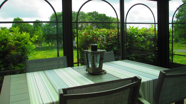 A conservatory with a table and chairs, large windows, and a view of greenery.