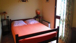 A bedroom with a bed, a nightstand with a lamp, a radiator, and a window with curtains.