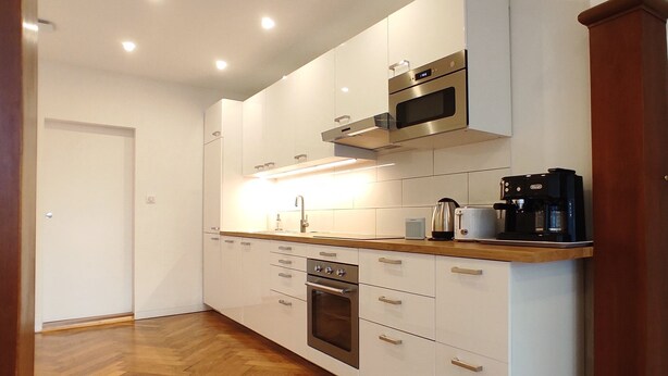 A modern kitchen with white cabinets, stainless steel appliances, and a wooden countertop.