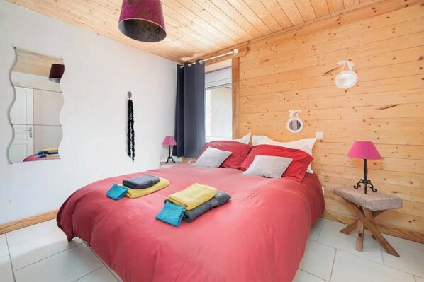 A bedroom with a wooden ceiling, a large bed with red bedding, two bedside lamps, and a small table with a lamp. - Private swimming pool, Jacuzzi and Sauna Clair de Lune 4**** (Uzemain)
