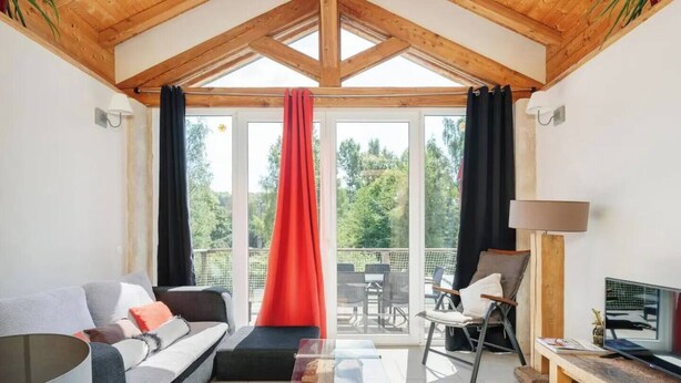 A cozy living room with a sofa, a coffee table, and a TV. There is a balcony with outdoor furniture and a red curtain. - Private swimming pool, Jacuzzi and Sauna Clair de Lune 4****  (Uzemain)