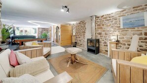 A cozy living room with a pool table, comfortable seating, a stone wall, and a wood-burning stove. - Private swimming pool, Jacuzzi and Sauna Clair de Lune 4****  (Uzemain)