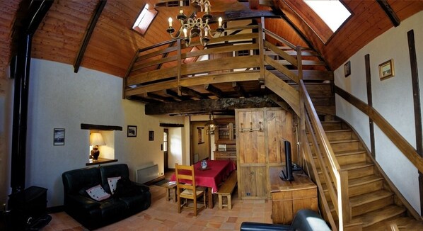 Amplia habitación estilo loft con escalera de madera, comedor y zona de estar acogedora.