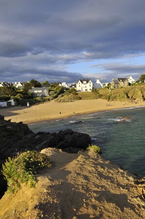 A coastal beach with houses in the background, a sandy shore, and rocky outcrops.