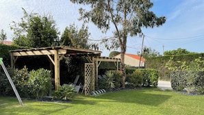A covered patio area with a pergola, surrounded by well-maintained grass and various plants.