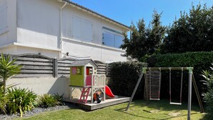 A residential backyard with a playhouse, swing set, and a small slide.
