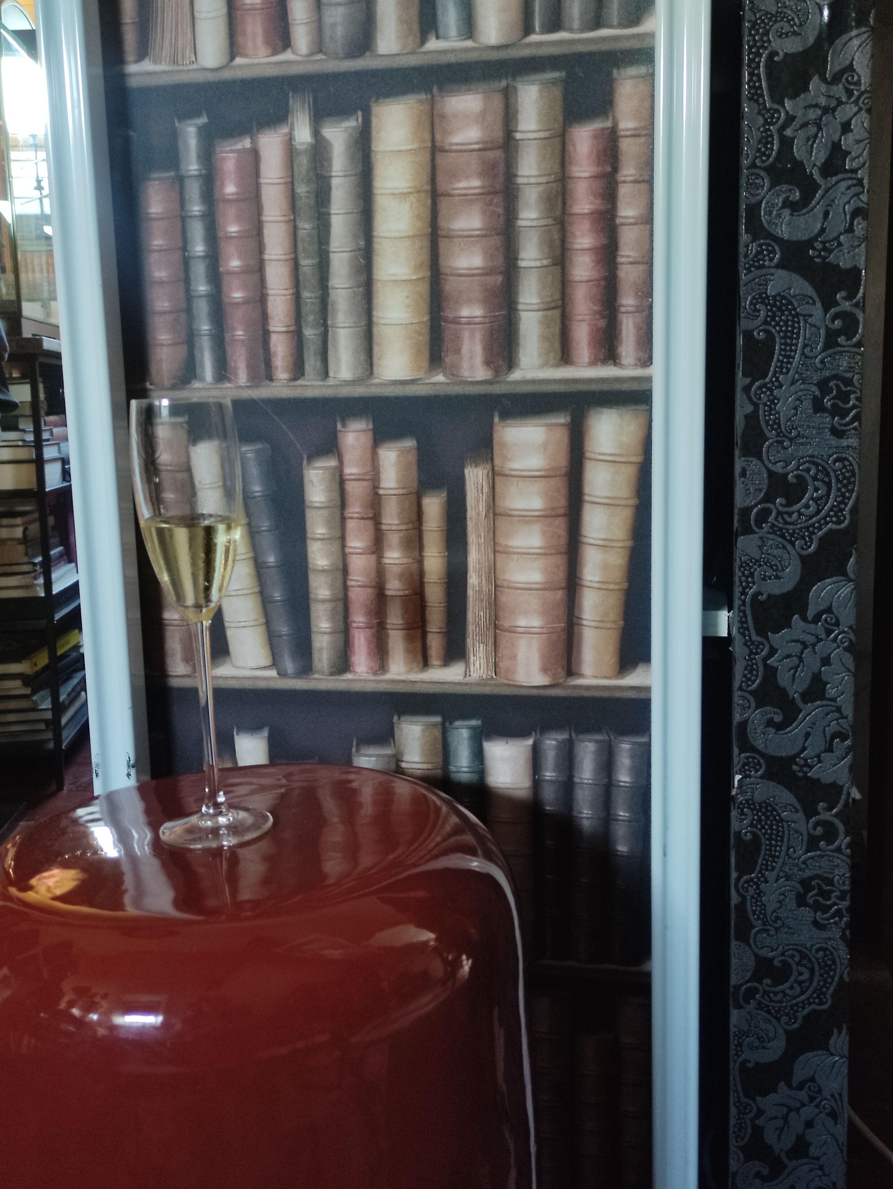 A bookshelf filled with books, a glass of wine, and a red ottoman.