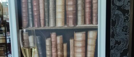 A bookshelf filled with books, a glass of wine, and a red ottoman.
