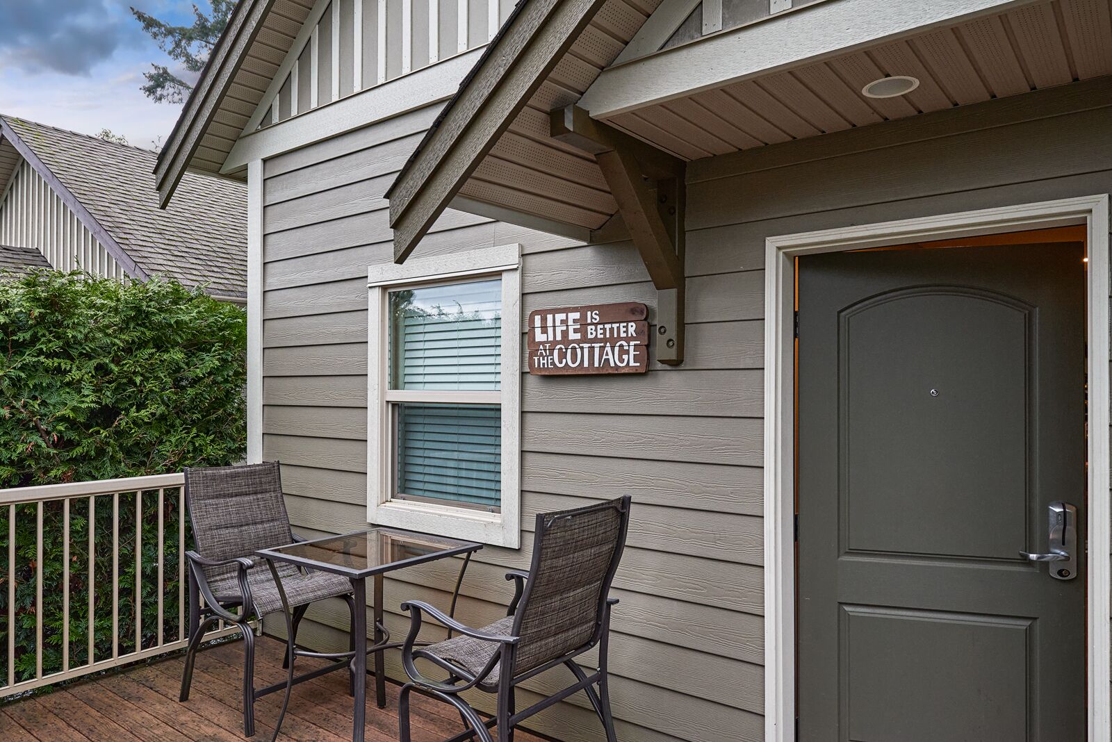 Un porche con dos sillones de mimbre, una mesa, una puerta y un cartel que dice 'Life is better at the cottage'.