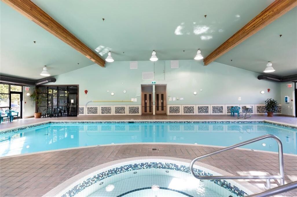 Une piscine intérieure avec un sol carrelé, un jacuzzi et des poutres en bois au plafond.