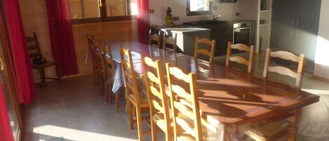 Un comedor con una mesa grande y sillas, una cocina al fondo y una ventana con cortinas.