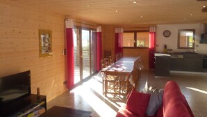 Interior de una cabaña de madera con comedor, cocina y un sofá rojo.