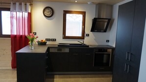 Cocina moderna con armarios negros, horno empotrado y ventana con cortina.