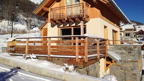 Eine Holzchalet mit Balkon, einer Steinsäule und einem mit Schnee bedeckten Dach.
