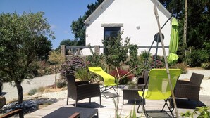 An outdoor patio with wicker furniture, a table, and a white building in the background.