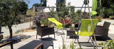 An outdoor patio with wicker furniture, a table, and a white building in the background.