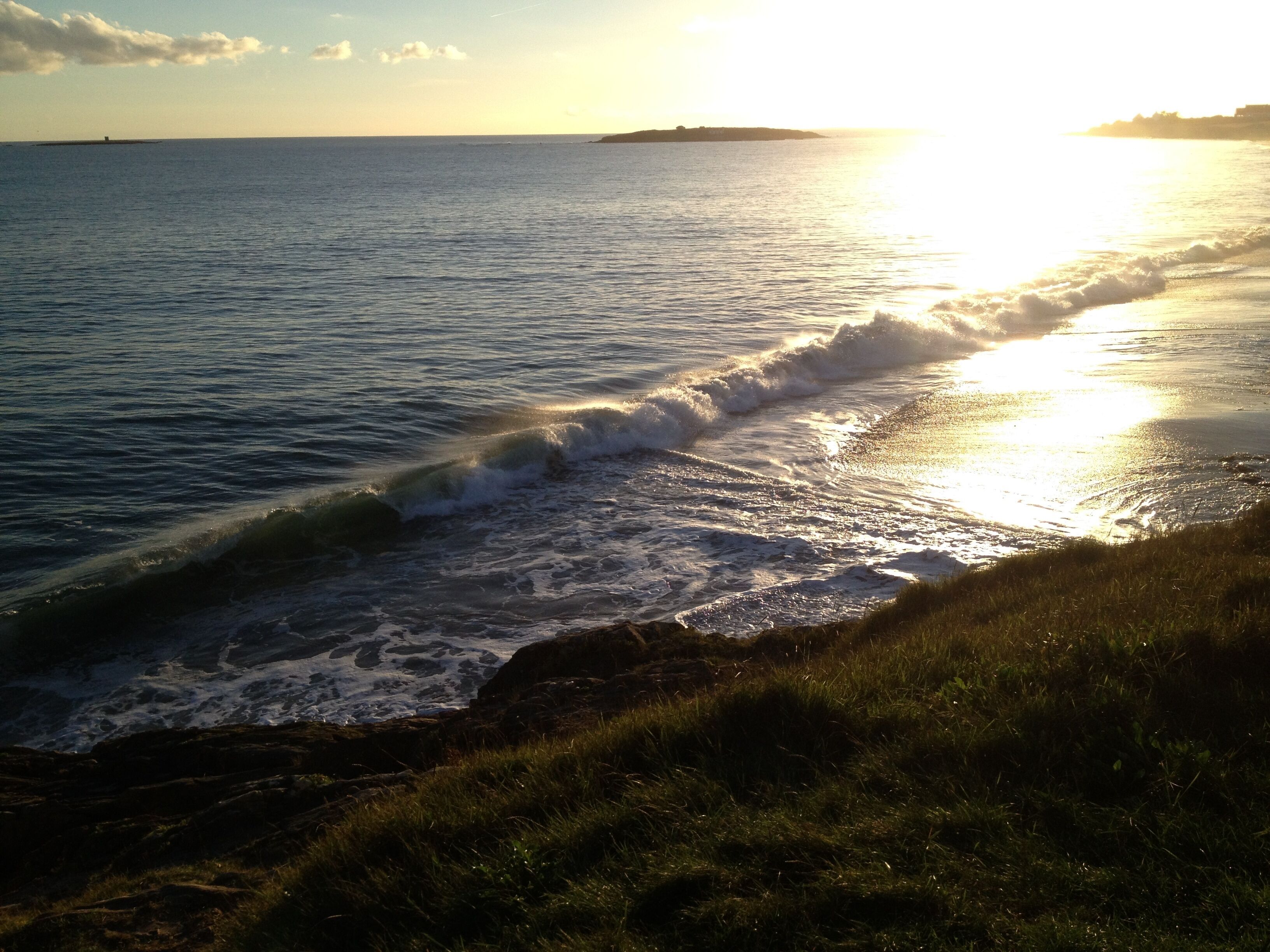 A coastal scene with waves crashing onto the shore, a clear sky, and a distant landmass.